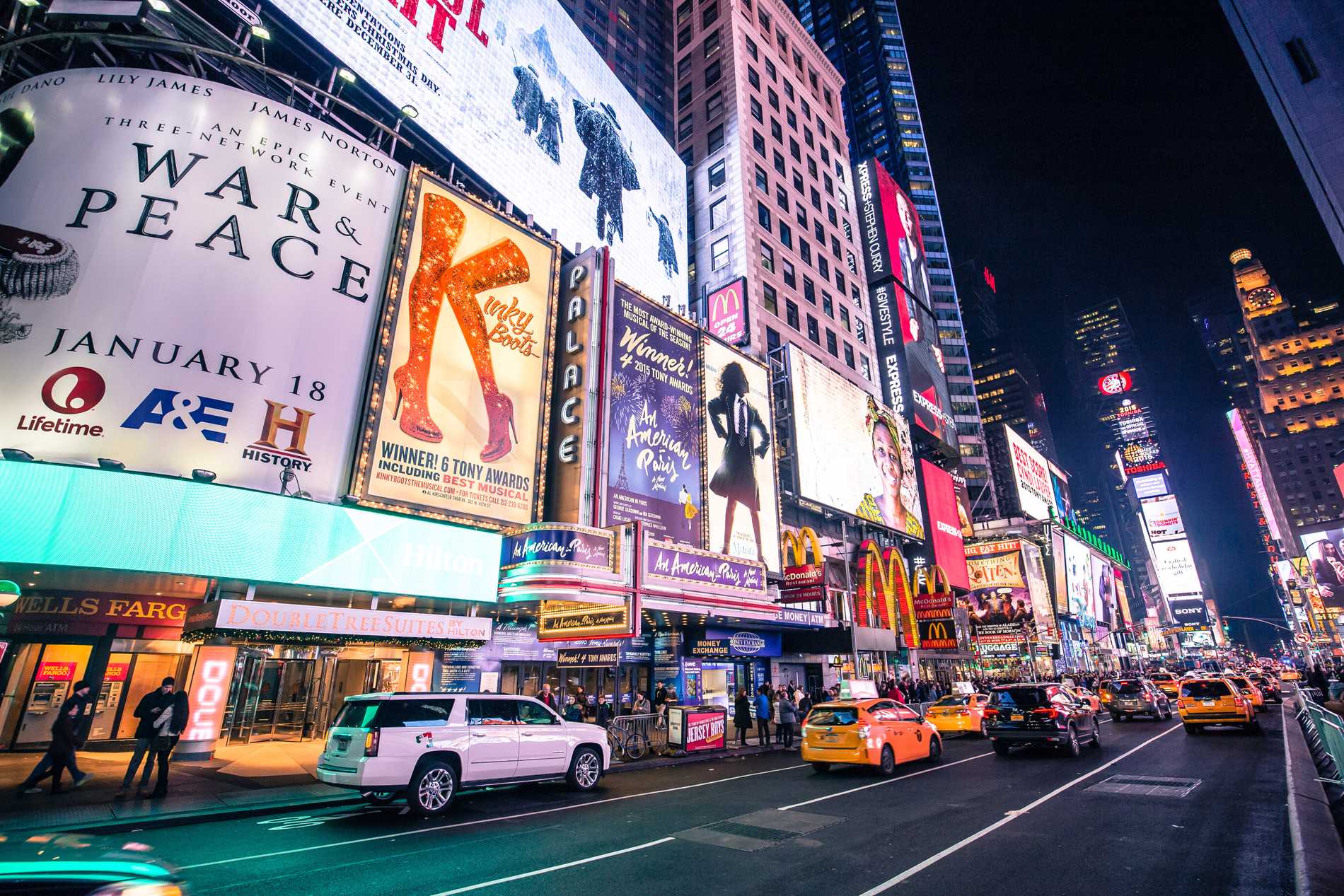 The bright lights advertising plays and musicals on Broadway as yellow taxis drive past below.