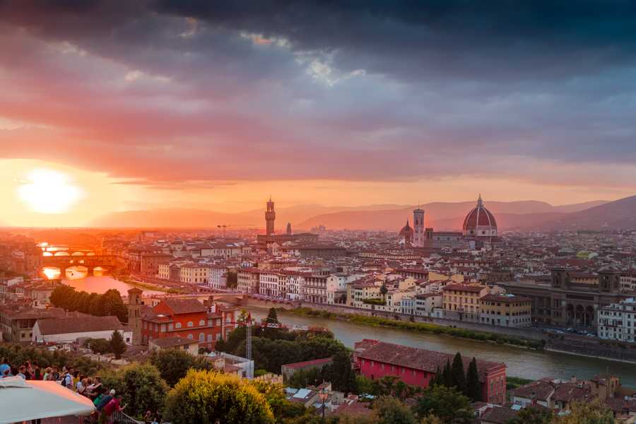 The sun sets over Florence, reflecting on the Arno River as it flows under the Ponte Vecchio.