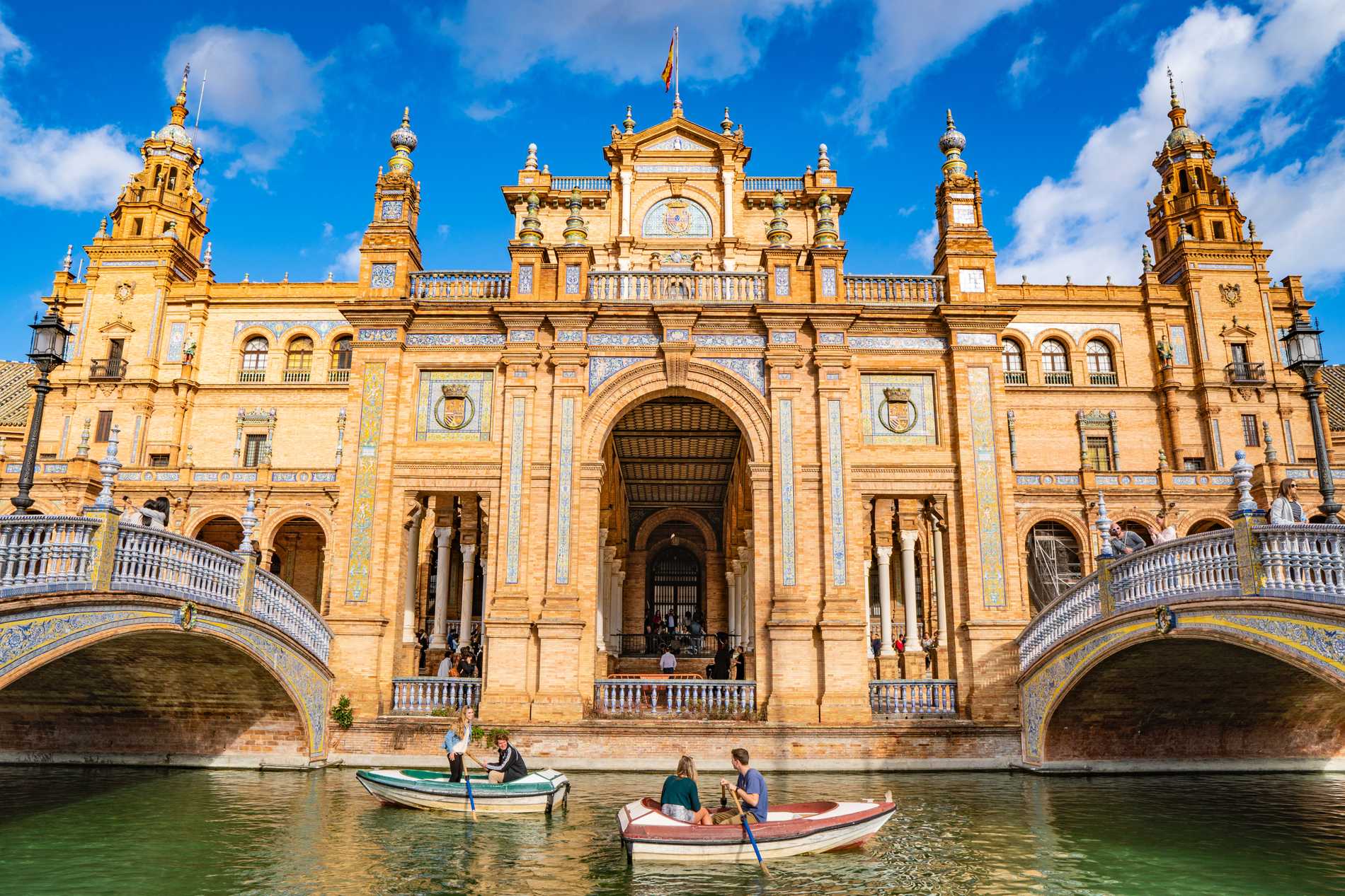 People in boats in front of the elaborate facade of the Plaza de España.