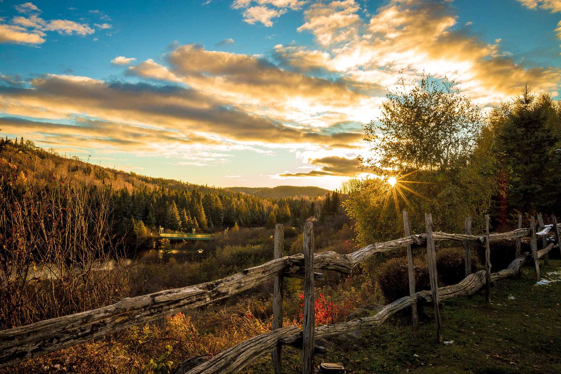 The sun sets through the trees on Autoroute des Laurentides, Prévost, turning the rolling hills and trees a golden hue.