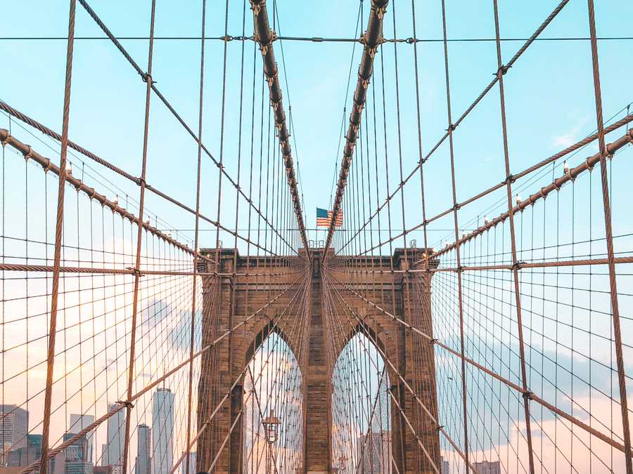 Looking up to the centre of the Brooklyn Bridge with the Stars and Stripes flying on top.